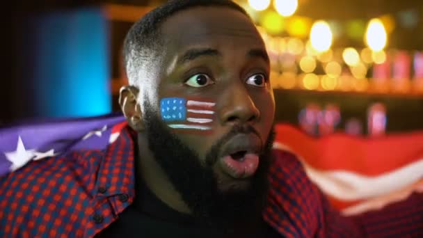Emotionaler afrikanisch-amerikanischer Fußballfan schwenkt Nationalflagge und jubelt dem Team zu — Stockvideo