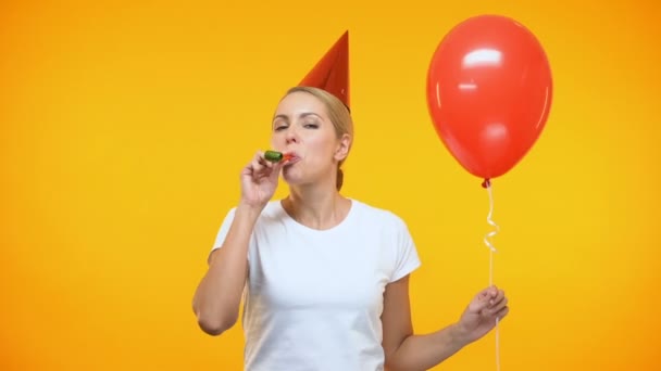 Joyeux jeune femme dans le chapeau de fête corne soufflante, tenant ballon rouge, anniversaire — Video