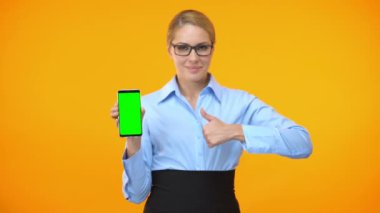Yeşil ekranlı akıllı telefonu tutan başparmakları gösteren kadın şirket çalışanı