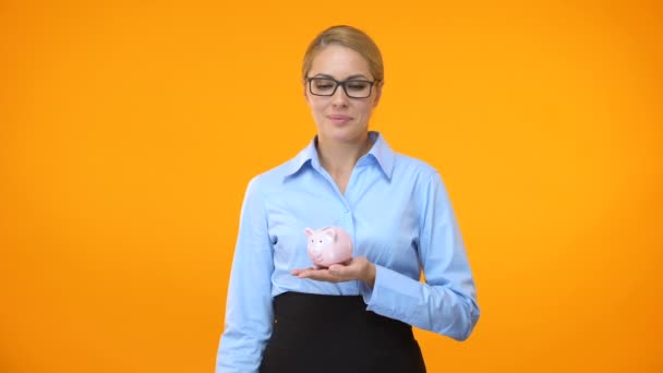 Sorrindo senhora de negócios colocando moeda piggybank fundo brilhante, depósito bancário — Vídeo de Stock