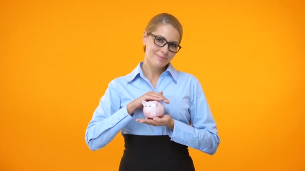 Feminino gerente de banco segurando piggybank na mão, fundo de pensão, seguro de depósito — Vídeo de Stock