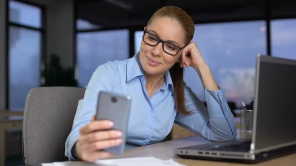 Женщина печатает сообщения на мобильном телефоне вместо того, чтобы работать, скучать на нелюбимой работе — стоковое видео