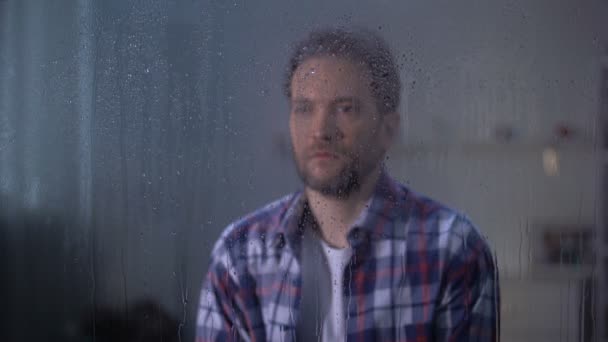 Lonely sad middle-aged man looking through rainy window, bad weather conditions — Stock Video