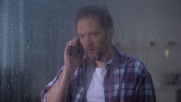 Homem chocado falando telefone atrás de janela chuvosa, notícias horríveis, morte relativa — Vídeo de Stock