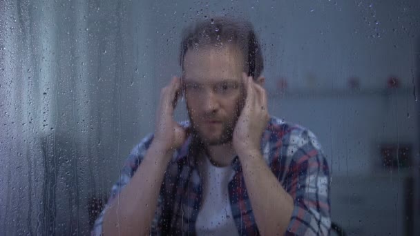 雨の窓の後ろの寺院をマッサージする疲れた中年の男、片頭痛 — ストック動画