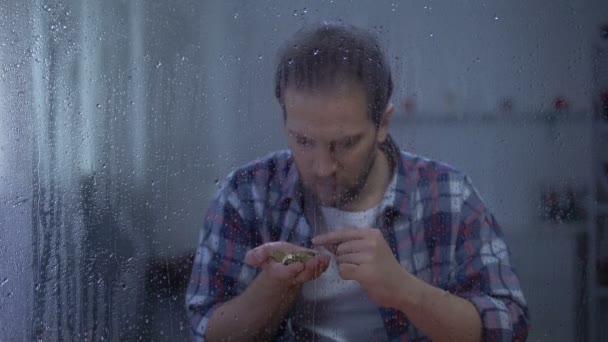 Hombre deprimido contando monedas detrás de ventana lluviosa, bajos ingresos, concepto de pobreza — Vídeos de Stock