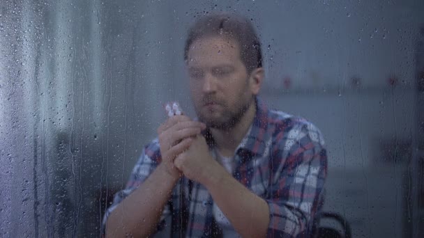 Hombre enfermo leyendo píldoras forma de dosificación detrás de la ventana lluviosa preocupándose por el efecto secundario — Vídeo de stock