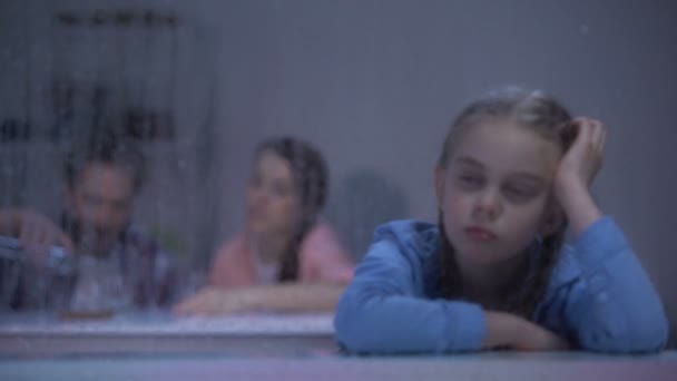雨の窓を見て動揺した女の子、背景にウォッカを飲む両親 — ストック動画