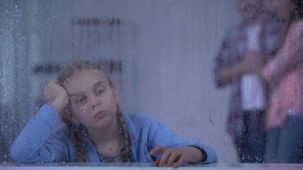 Niño huérfano triste cerca de la ventana lluviosa, padres adoptivos tomando chica del orfanato — Vídeos de Stock