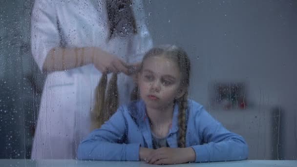 雨の窓の後ろに小さな女の子の髪を編む乳母、孤児院でのケア、美しさ — ストック動画