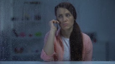 Yağmurlu pencerearkasında telefon konuşan üzgün orta yaşlı bayan, kötü haber, konuşma