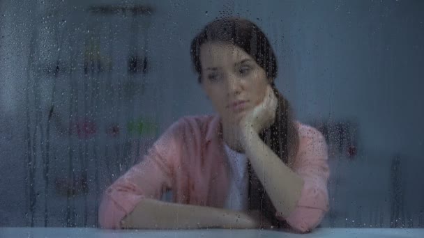 Deprimida jovem mulher olhando para a câmera através de janela chuvosa, problemas de vida — Vídeo de Stock