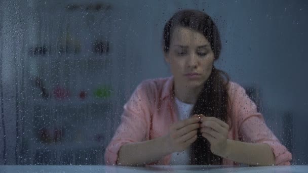 Disappointed female holding engagement ring behind rainy window, divorce concept — Stock Video