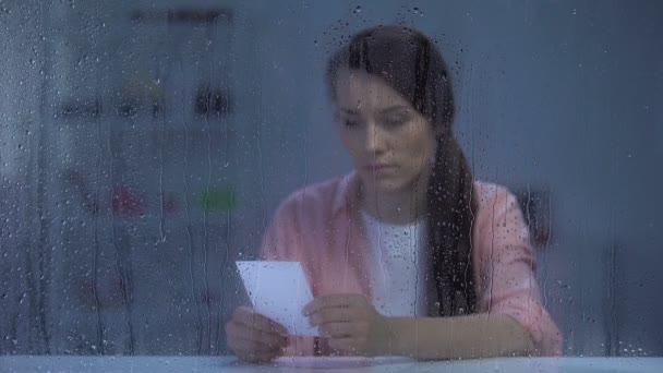 Αναστατωμένη γυναίκα κοιτάζοντας φωτογραφία πίσω από βροχερό παράθυρο, αγνοούμενος σύζυγος μετά το διαζύγιο — Αρχείο Βίντεο