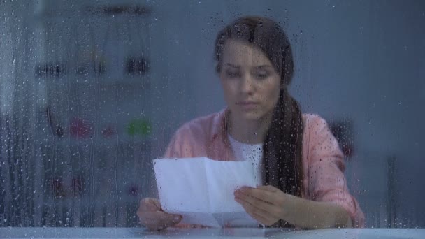 Upset female reading letter behind rainy window, bad news from relatives — Stock Video