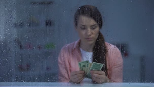 雨の窓の後ろにお金を数える中年の女性、貧しい予算、貧困 — ストック動画