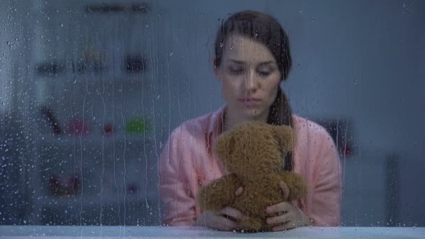 Hopeless middle-aged woman holding teddy bear, looking for support, rainy day — Stock Video