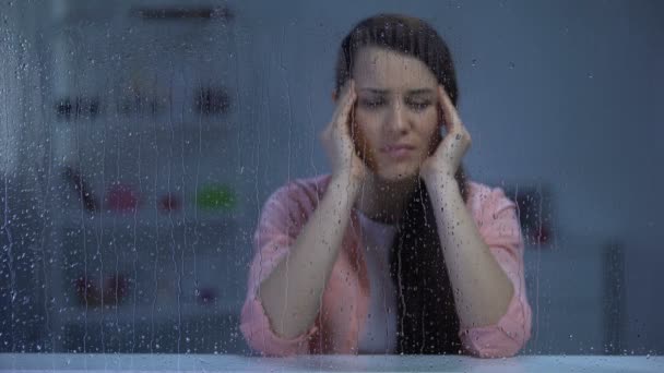 Виснажена жінка, яка страждає від головного болю за дощовим вікном, розлад мігрені — стокове відео