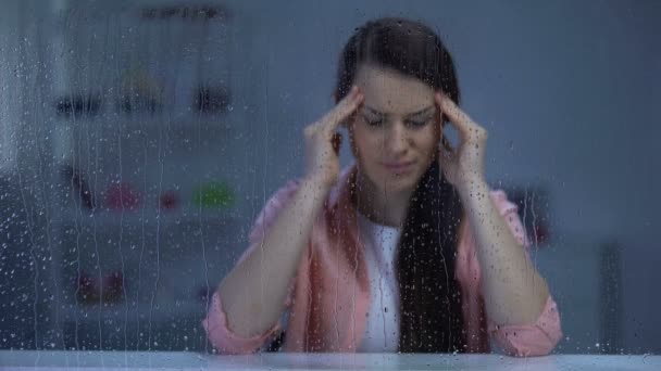 Dame d'âge moyen épuisée massant les temples derrière la fenêtre pluvieuse, douleur migraine — Video