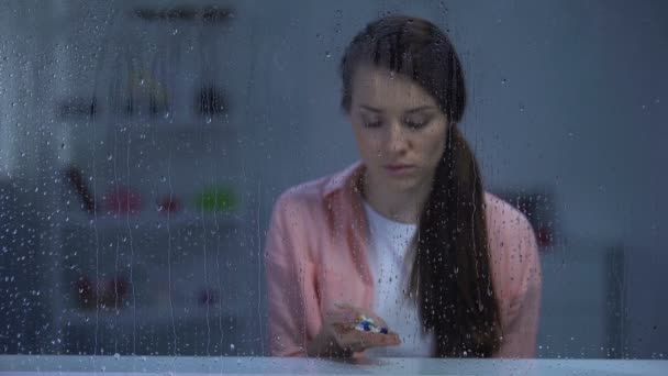 Upset woman holding pills in palm behind rainy window, expensive medicine — Stock Video