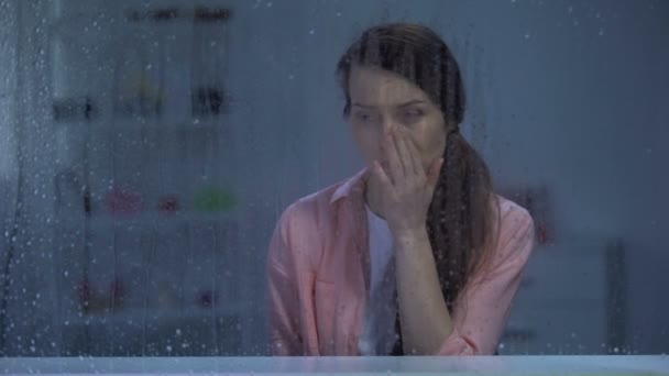 Плаче жінка середнього віку, яка дивиться крізь дощове вікно, проблеми зі здоров'ям та життям — стокове відео