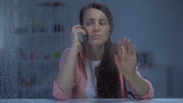 Mujer hablando por teléfono y mirando por la ventana de lluvia, esperando marido por la noche — Vídeo de stock