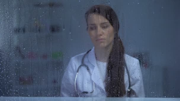 Женщина-врач со стетоскопом подавлена после смерти пациента, дождливая погода — стоковое видео