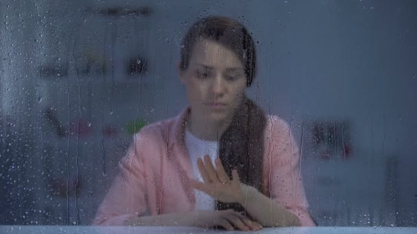 Woman taking off engagement ring behind rainy window, upset after break up — Stock Video