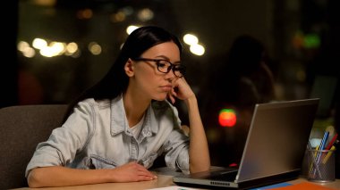 Young woman bored working on laptop in office, lacking motivation, unloved job clipart