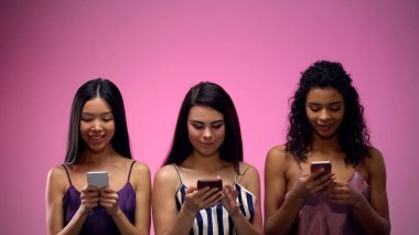 Üç çok ırklı kadın pembe arka plan üzerinde akıllı telefon kaydırma, metin için yer