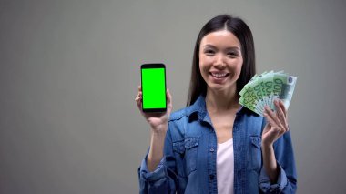 Gülümseyen Asyalı kadın akıllı telefon ve euro tutan, online çalışma, cashback