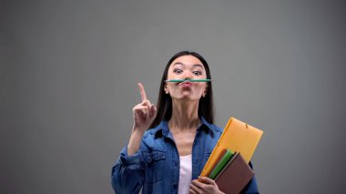 Not defterleri olan kız öğrenci. Dudaklı kalem tutarken eğleniyor. Yaratıcılık.