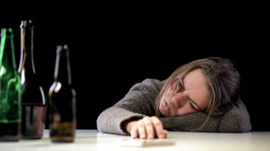Alkol şişeleri, umutsuzluk şişeleri yanında masada yatan bağımlı zayıf iradeli kadın