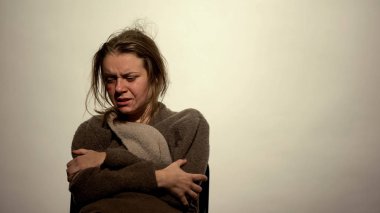 Yüzü morarmış, beyaz arka planda oturan genç bir kadın, uyuşturucu bağımlısı.