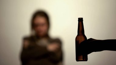 Elinde bira şişesi alkol içmek için sunan, arka planda bağımlısı kadın