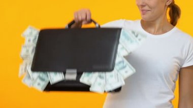 Woman showing brief case full of money into camera, start-up investing capital