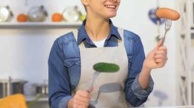 Elinde sosis ve salatalık ile çatal tutan önlük gülümseyen kız, seçim