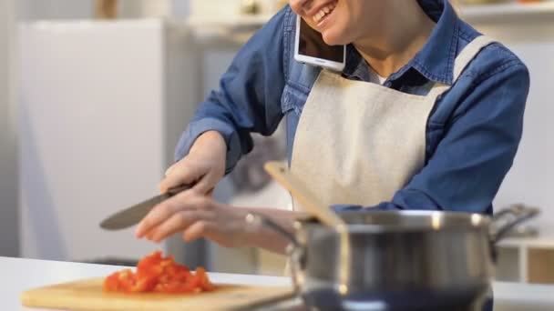 Dona de casa cortando tomate e adicionando em panela enquanto fala no celular — Vídeo de Stock