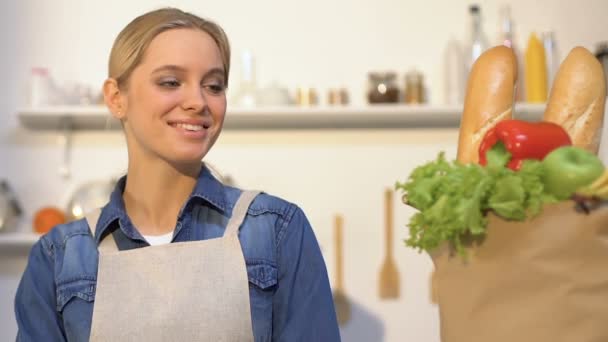 Smiling woman looking at paper bag with fresh bread, fruits and vegetables — Stock Video