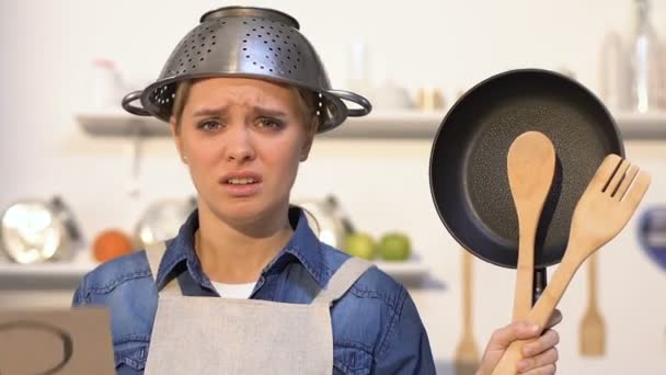 Señora sin experiencia con colador en la cabeza sosteniendo los servicios públicos de cocina y ayudar a firmar — Vídeo de stock