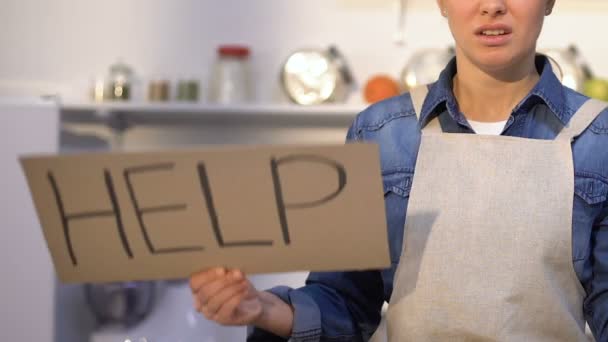 Mujer trastornada en delantal de pie en la cocina y sosteniendo el cartel de ayuda, nuevo en la cocina — Vídeo de stock