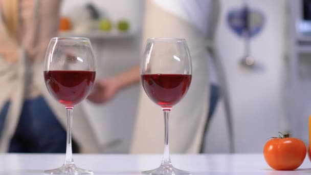 Verres à vin sur la table de cuisine, couple heureux dansant sur le fond, romance — Video