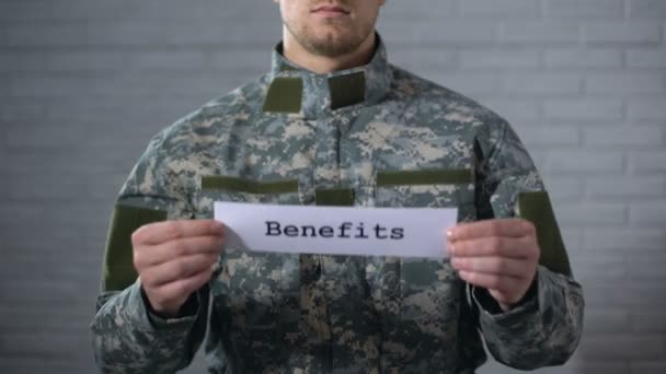 Prestaciones palabra escrita en el signo en las manos de soldado masculino, veteranos de apoyo, ayuda — Vídeos de Stock