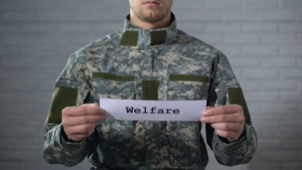 Palavra de bem-estar escrito no sinal em mãos de soldado masculino, ajuda financeira, apoio — Vídeo de Stock