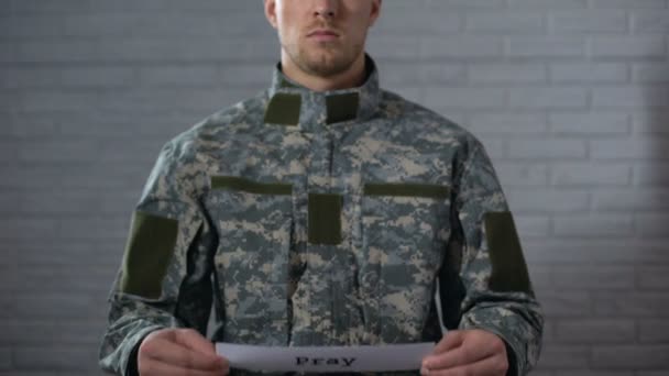 Ore a palavra escrita no sinal nas mãos do soldado masculino, serviceman pedindo a paz — Vídeo de Stock