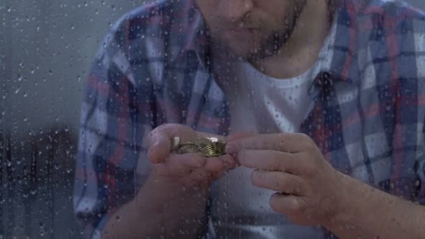 Depresif orta yaşlı adam sikke sayma, yağmurlu pencereden kamera bakıyor — Stok video