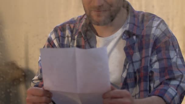 Человек читает письмо за мокрым окном, солнечные лучи сияют, вера в лучшее, надежда — стоковое видео
