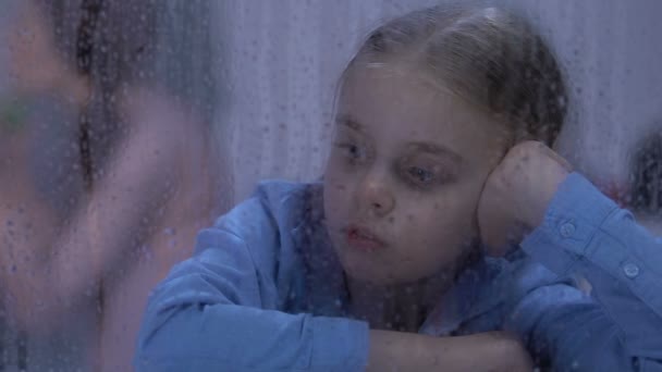 Dochter op zoek in regenachtige venster, ouders ruziën op achtergrond, conflict — Stockvideo