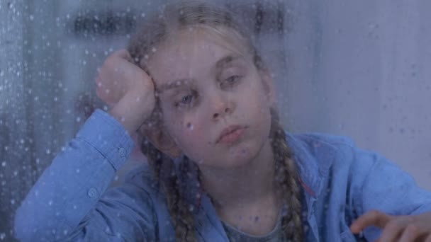 Ledsen föräldralös flicka tittar på regn, par stående bakom, fosterfamilj Coming — Stockvideo