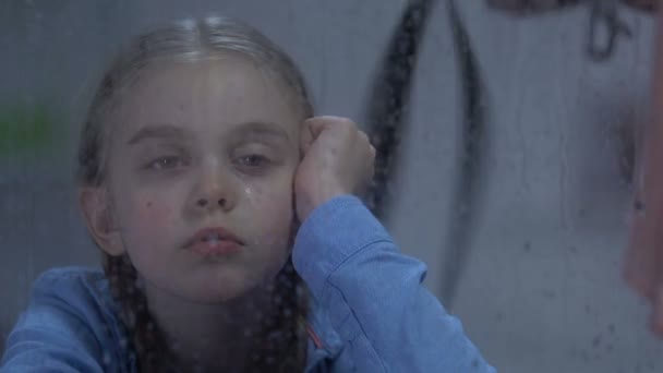 Грустная плачущая девушка смотрит в дождливое окно, леди кричит и угрожает поясом — стоковое видео